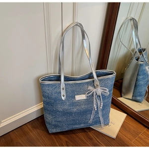 Detail of blue denim tote bag with silver leather trim and lace pearl bow pendant