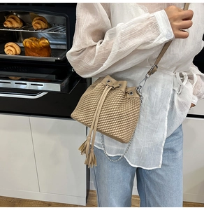 Detail of woven texture beige bucket bag with drawstring closure and tassel accent