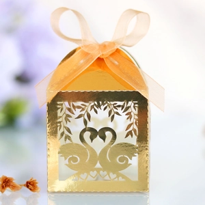 Close-up of golden laser-cut wedding favor box with swan heart design and ribbon