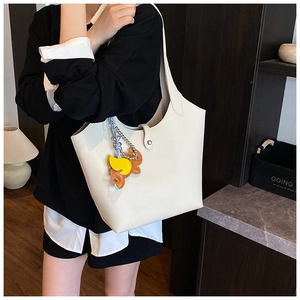 Close-up of a white leather tote bag with a small horse charm in a casual urban setting