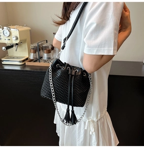 Detail of black woven bucket bag with elegant leather tassels and metal chain strap