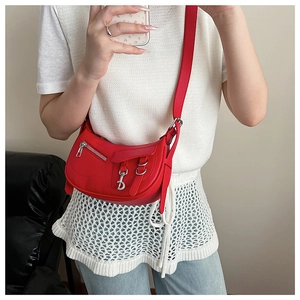 Detail of red lychee pattern leather saddle bag featuring silver D pendant and zip