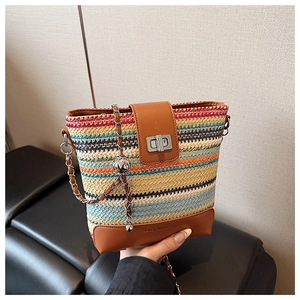 Detail of colorful woven straw bucket bag with brown leather flap and silver chain strap