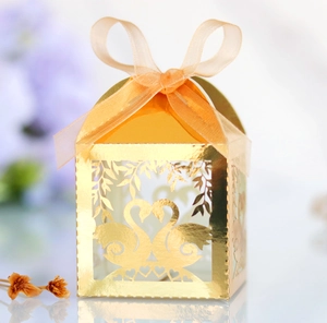 Detail of laser-cut gold wedding favor box with swan heart design and orange ribbon