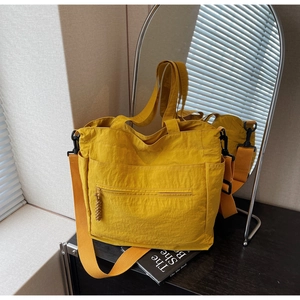 Detailed close-up of a large yellow nylon tote bag with functional pockets and wide strap