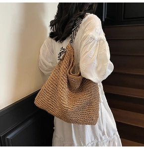 Detail of woven straw tote bag featuring black and white striped ribbon shoulder straps