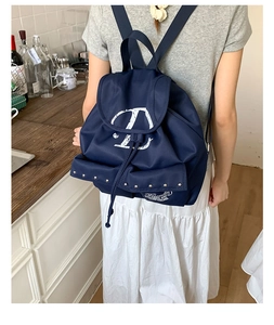 Détail du sac à dos en nylon bleu foncé avec logo blanc et rivets sur la poche frontale