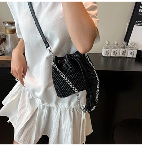 Detail of black woven bucket bag with drawstring closure and silver chain tassel strap