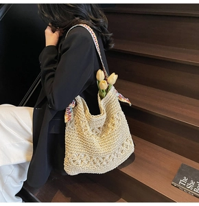 Close-up of beige hollow crochet hobo bag with colorful embroidered ethnic strap on stairs