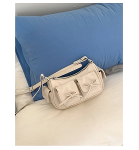 Vue détaillée du sac bandoulière en cuir crème avec poches à rabat ornées de nœuds