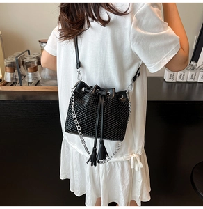 Detail of black woven bucket bag with drawstring tassels and silver chain strap