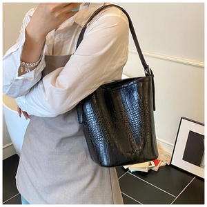 Detail of black crocodile pattern bucket bag with wide shoulder strap and polished finish