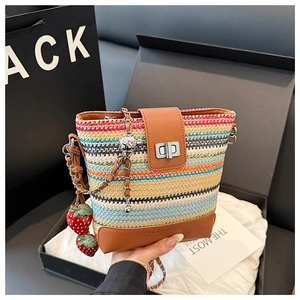 Detail of colorful striped straw bucket bag with leather flap and strawberry charm