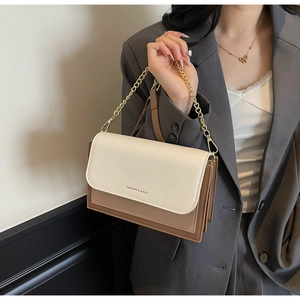 Chic beige and caramel crossbody bag with gold chain strap worn over a grey blazer