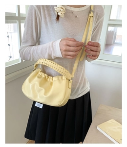 Close-up of pale yellow ruched cloud bag with woven handle and adjustable strap worn by model