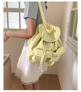 Detailed view of yellow nylon backpack featuring rivet pockets and white letter D print