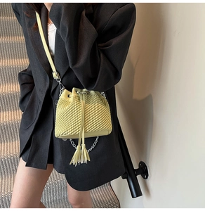 Close-up of yellow woven bucket bag featuring drawstring closure and tassel detail