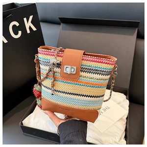 Detail of colorful woven straw bucket bag with strawberry charm and metal chain strap