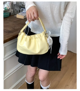 Close-up of lemon yellow pleated cloud bag with woven handle and pearl bow pendant