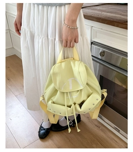 Détail d'un sac à dos en nylon jaune clair avec lettre D blanche et clous argentés