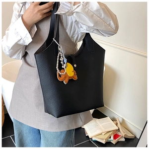 Detail of black lychee grain leather tote bag with orange elephant charm and pearl strap