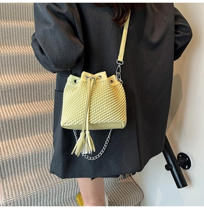 Close-up of woven bucket bag in grass green with tassel detail and silver chain