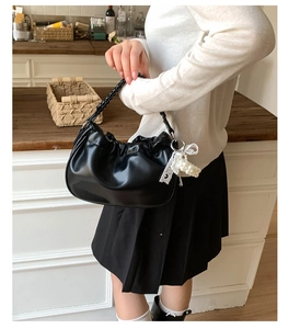 Detail of black pleated cloud bag with woven handle and pearl lace charm on wooden table