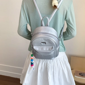 Détail d'un mini sac à dos argenté avec pendentif en perles et texture litchi métallique