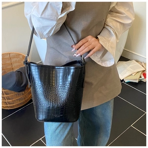 Detail of black crocodile texture bucket bag with adjustable shoulder strap and brand logo