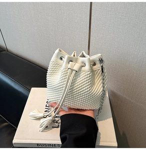 Detailed view of white woven bucket bag with drawstring closure and silver chain strap