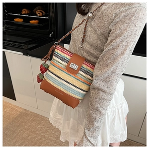 Detail of colorful woven straw bucket bag featuring red strawberry charms and metal chain