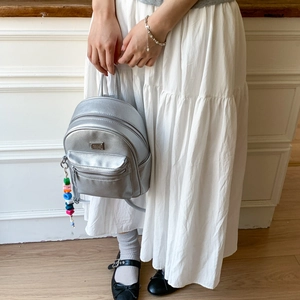 Détail du mini sac à dos argenté montrant le similicuir grainé et le charm coloré