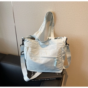 Macro shot of light blue nylon tote bag showing zipper pocket and side storage details