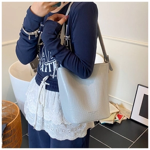 Detail of light blue crocodile pattern bucket bag with adjustable shoulder strap and debossed text