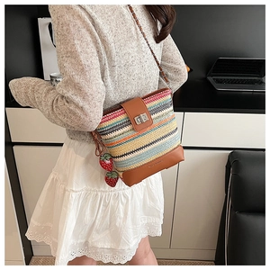 Detail of a woven bucket bag with vibrant stripes, strawberry charms and a metal twist lock