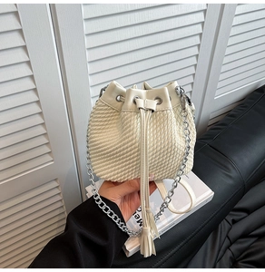 Detail of cream bucket bag with woven texture, drawstring closure and silver chain strap