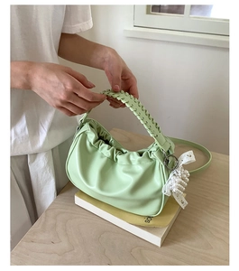 Close-up of light green ruched bag with woven handle, pearl charms, and lace bow