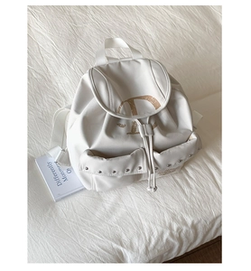 Détail du sac à dos crème avec fermeture à cordon et poches à rivets sur toile robuste
