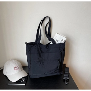 Detail view of a black nylon tote bag with a front zipper pocket and removable shoulder strap