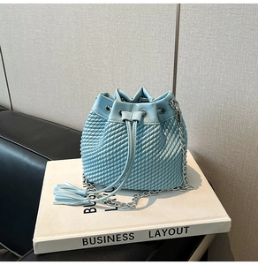 Detail of light blue woven bucket bag with drawstring closure and silver chain strap