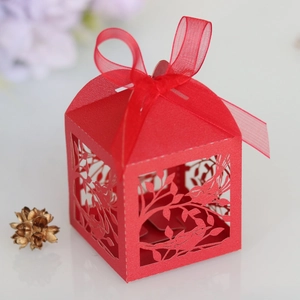 Detail of red laser-cut wedding favor box with bird patterns and organza ribbon