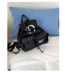Détail du sac à dos en nylon noir avec clous argentés et logo D sur literie blanche