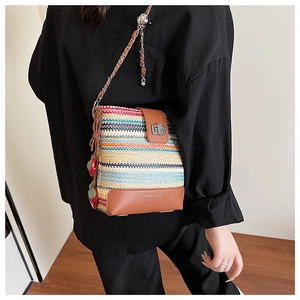 Detail of colorful woven straw bucket bag with leather flap and strawberry charms
