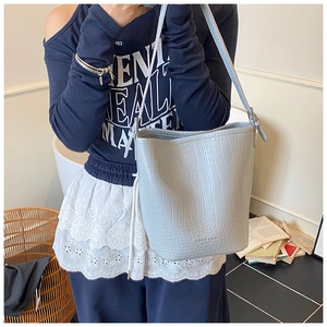Detail showing crocodile pattern texture and leather logo on grey blue bucket bag