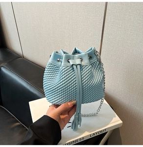 Macro view of light blue bucket bag with woven texture, drawstring tassels and chain strap