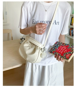 Detailed view of cream pleated cloud bag with woven handle and beaded charm accessory