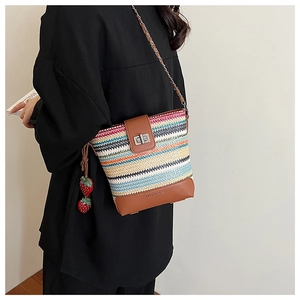 Detail of colorful woven straw bucket bag with brown leather trim and strawberry charm