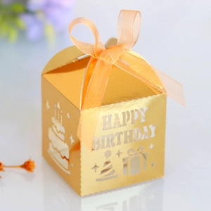 Detail of laser-cut 'HAPPY BIRTHDAY' golden treat box with orange ribbon and cake patterns