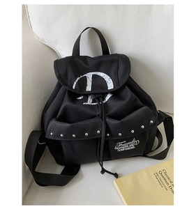 Détail du sac à dos en toile noire montrant des rivets métalliques et l'imprimé lettre D