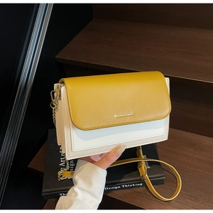Detail view of contrast leather crossbody bag with yellow strap and gold chain on wooden stairs